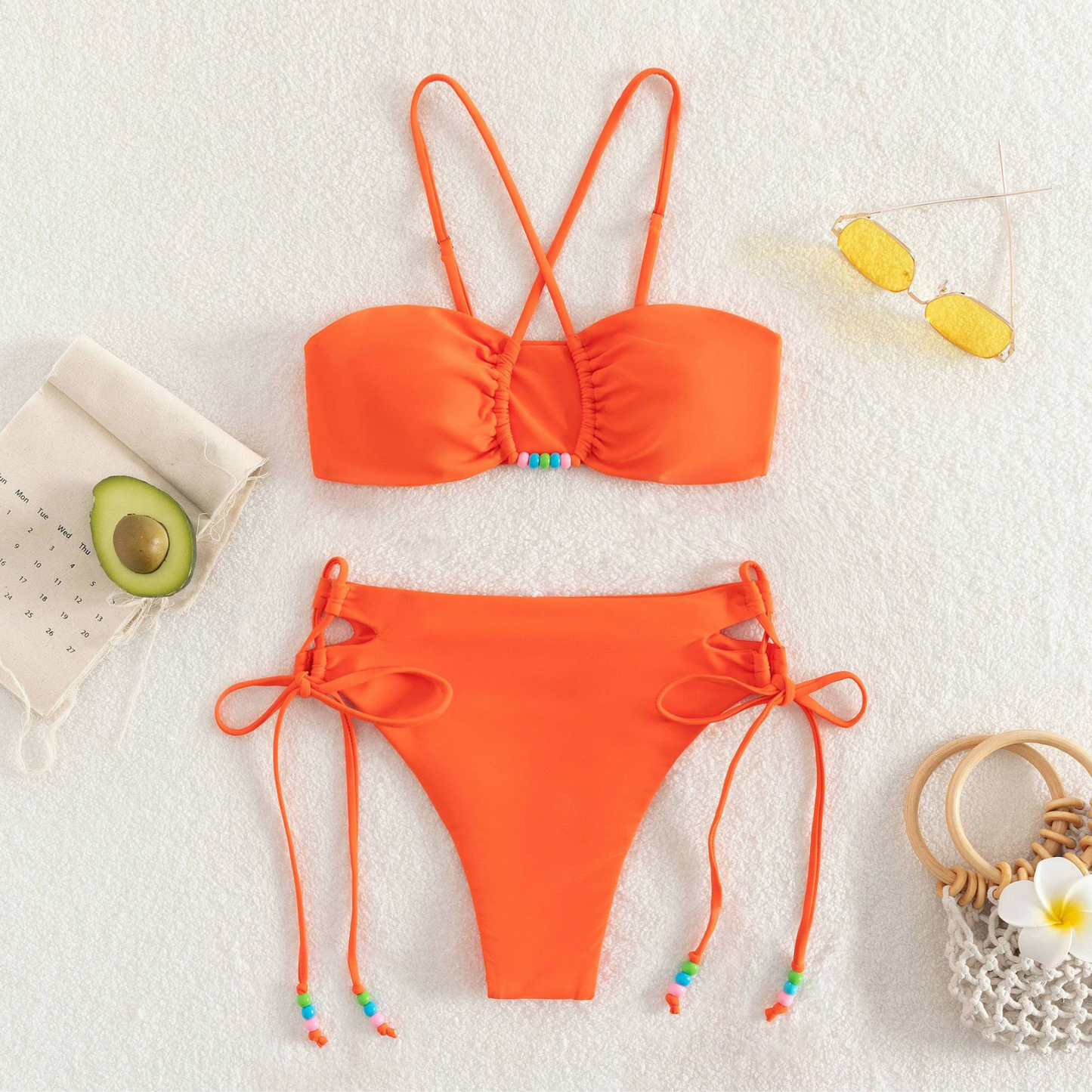 Orange two-piece bikini from Rita Rosa's Summer 2023 Collection. Solid color with bead charm and crisscross top. High-waisted, tie-side bottom accentuates curves