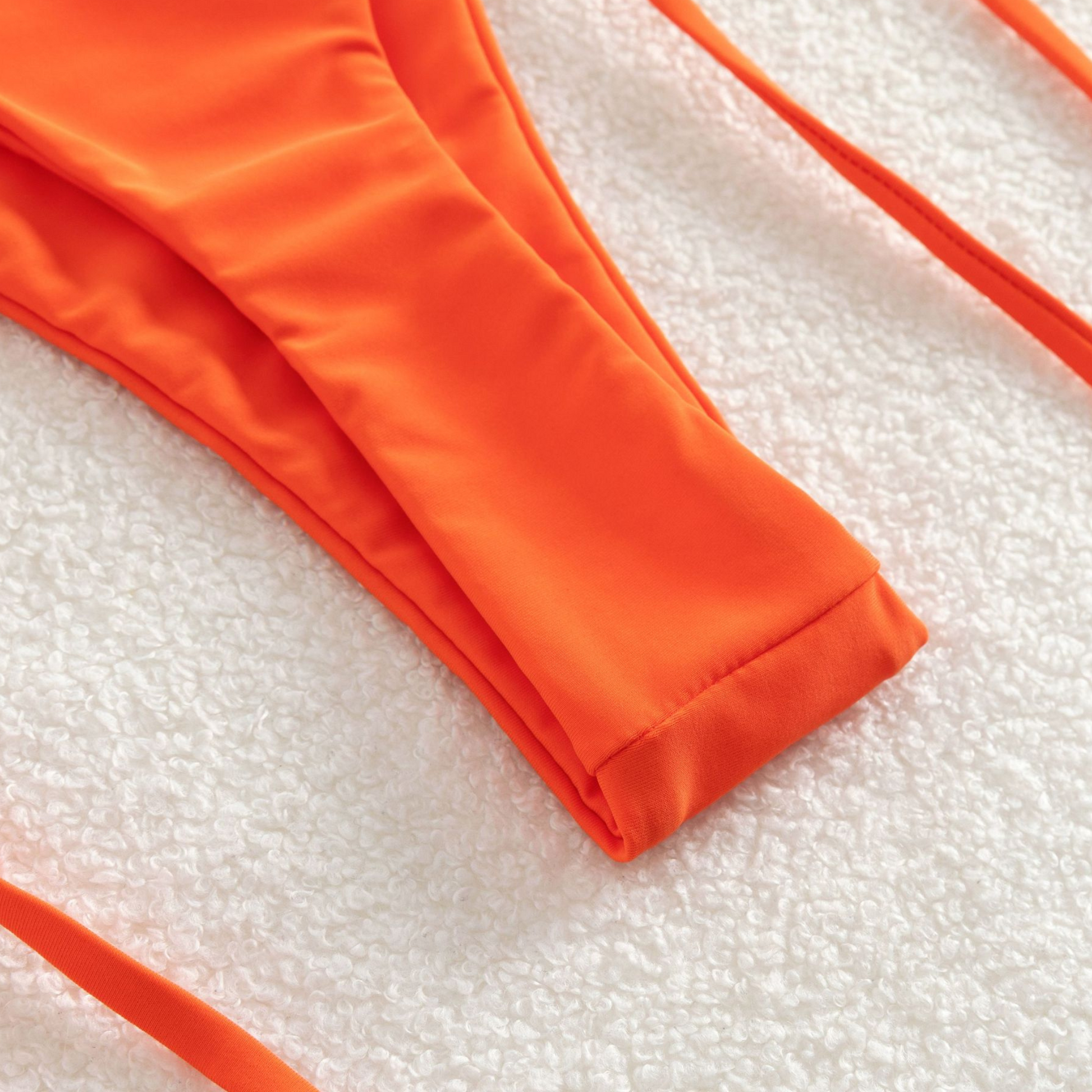 Orange two-piece bikini from Rita Rosa's Summer 2023 Collection. Solid color with bead charm and crisscross top. High-waisted, tie-side bottom accentuates curves